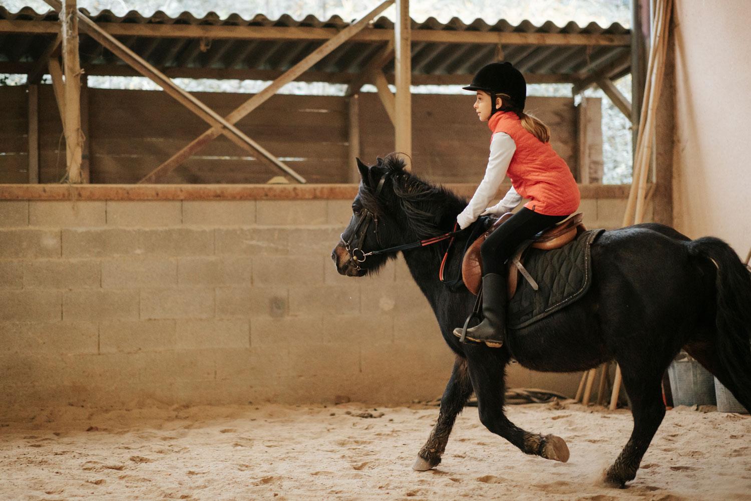 Une jeune fille est au trot sur un cheval dans le centre équestre du Couzon