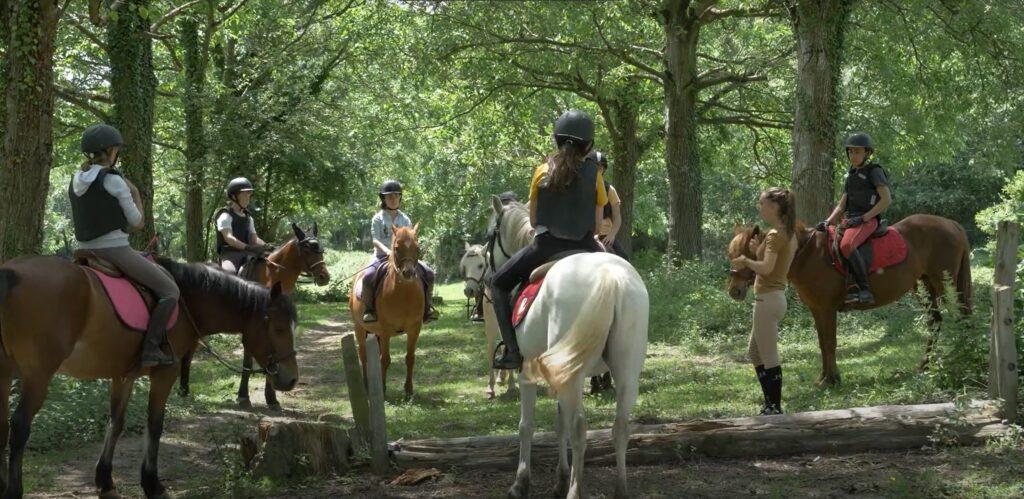 Une femme donne des instructions à des cavaliers sur leurs chevaux qui l'entourent au centre équestre du Couzon