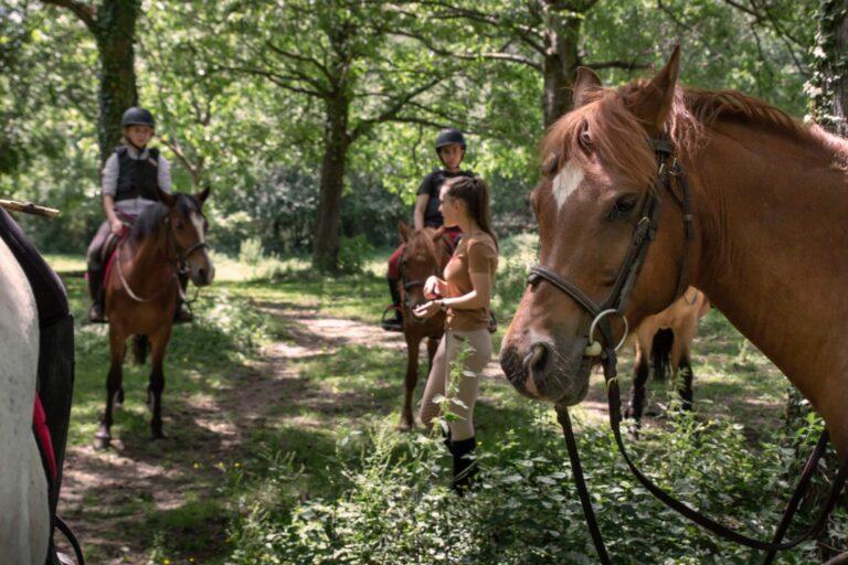 Une femme donne des instructions à des cavaliers sur leurs chevaux qui l'entourent au centre équestre du Couzon